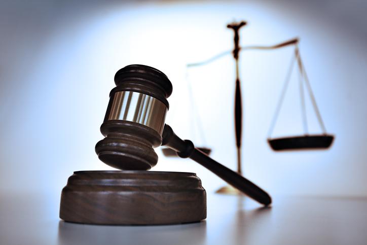 A close up of a gavel with a justice scale out of focus in the background. Photographed with a very shallow depth of field.